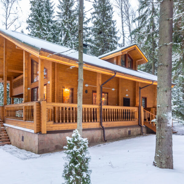 Snow-covered beautiful wooden house in the forest at dusk. Modern log cabin with large decks